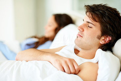 Young man sleeping on bed besides his wife at the back
