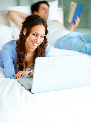 Couple on bed - Woman using laptop and man reading a book at the back