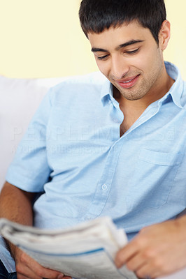 Relaxed young man reading newspaper while sitting on couch