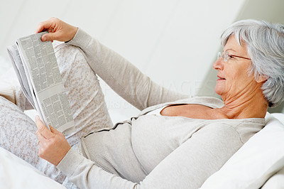 Retired senior woman reading newspaper on bed at home