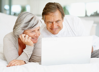 Old couple lying on the bed while using a laptop