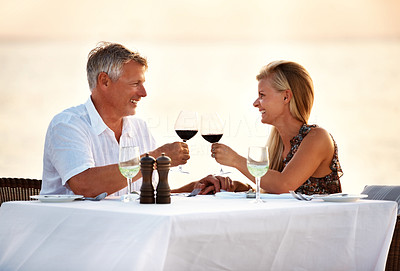 Romantic mature couple drinking wine in the beach during sunset