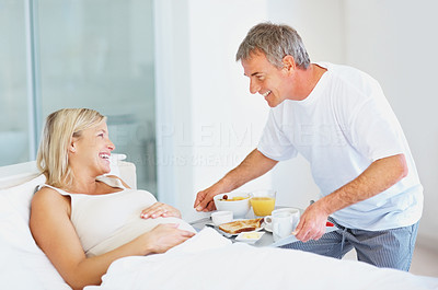 Husband serving breakfast to pregnant woman at the bed