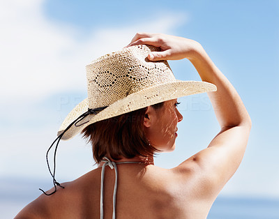 Rear view of a woman holding a hat to her head facing the sky