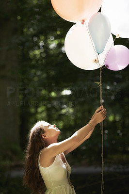 A pretty young woman holding a bunch of balloons in the forest