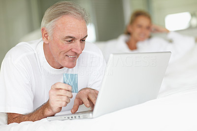 Elderly man lying on bed and shopping online with a credit card