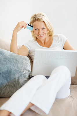A cute smiling mature woman with laptop and credit card on couch
