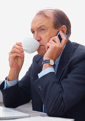 A senior business man using a phone while drinking