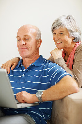 Happy senior woman watching her husband work on a laptop
