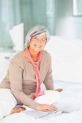 A relaxed old senior woman reading a newspaper at home