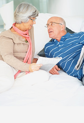 Senior man and woman holding newspapers while talking on bed