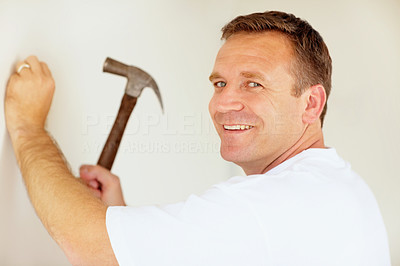 Smiling man hitting a nail into a wall using a hammer