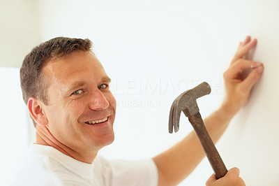 Portrait of a smiling mature man hammering a nail into a wall
