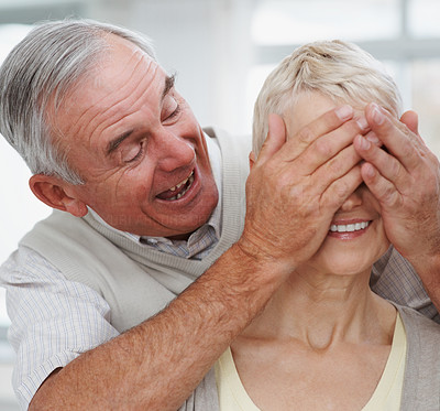 Happy elderly man covering wife\'s eyes surprising her