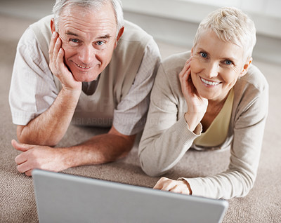 Senior couple with a laptop computer lying on the floor