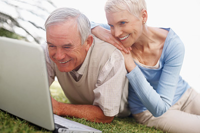 Happy senior couple using a laptop on grass