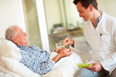 Doctor giving an old man a pill while at his bed