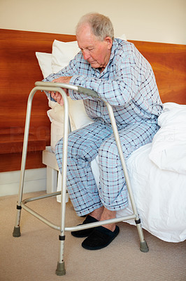 Sad elderly man sitting with a walker on his bed