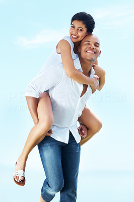 Playful young couple enjoying piggyback ride against sky