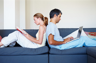 Couple sitting back to back, husband working on laptop while wife reading book