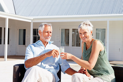 Senior couple enjoying a glass of champagne with their house at the back