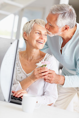 Senior man giving flower to wife while she\'s working on computer