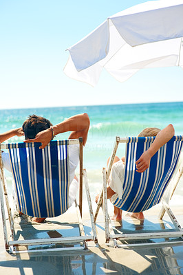 Rear view of a couple resting by the beach on a deck chair on a sunny day
