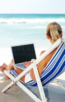 Young woman working on a laptop while relaxing on a beach