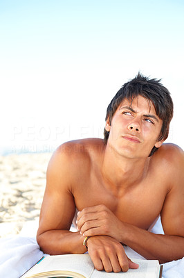 Young man by at the beach reading a book and looking away