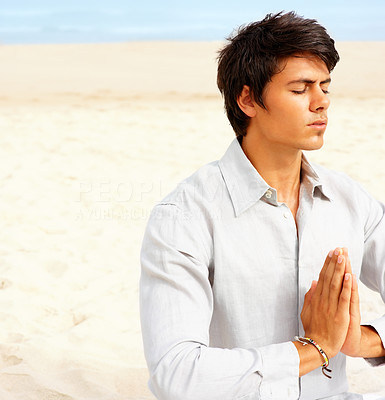 Young man meditating on the beach with his hands joined