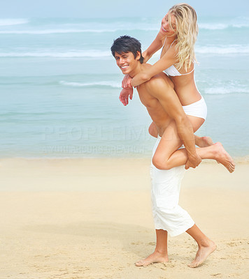 Handsome young man carrying his pretty girlfriend on his back at a beach