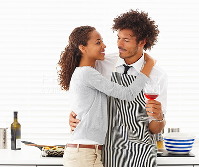 Man holding a glass of wine in the kitchen with his wife hugging him