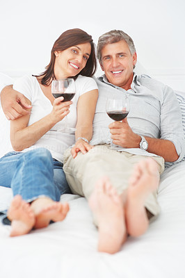 Cute mature couple lying on their bed enjoying a glass of wine