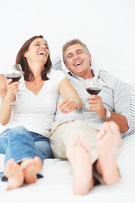 Laughing mature couple lying on their bed enjoying a glass of wine