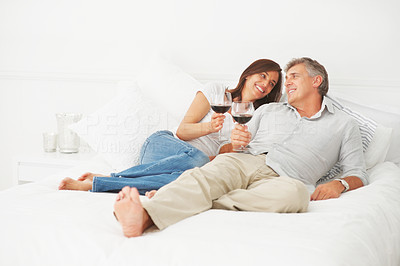 Happy mature couple lying on their bed having a glass of wine