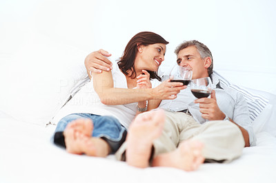 Charming mature couple lying on their bed having a glass of wine