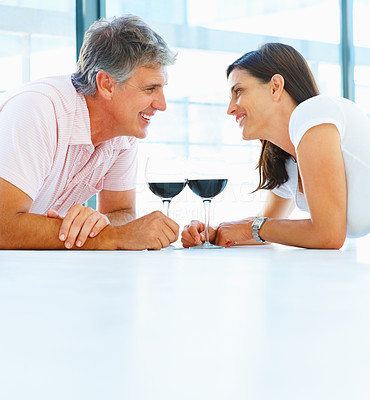 Cute mature couple lying down on the floor at home and having a glass of wine