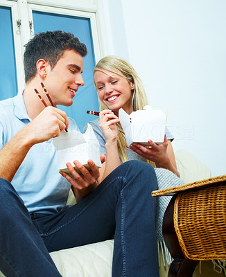 Young couple eating from a takeaway container with chopsticks