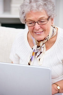 Closeup of a happy old woman sitting on sofa and using laptop at home