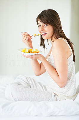 Happy young woman eating fruit salad at home