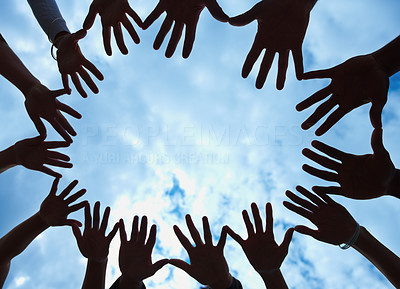 Circle of hands held out in unity against blue sky