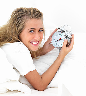 Closeup of young woman lying on bed and holding an alarm clock