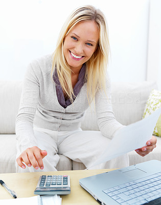 Portrait of a happy young woman sitting on sofa using laptop and calculator