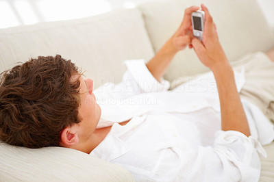 Young guy lying on sofa and using mobile phone
