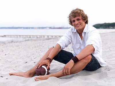 Young man sitting on beach with rugby ball