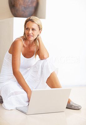 Thoughtful woman sitting on floor with laptop , looking away