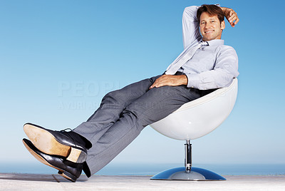 Relaxed businessman sitting on chair against sky