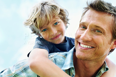 Smiling mature man giving piggyback ride to his son against sky