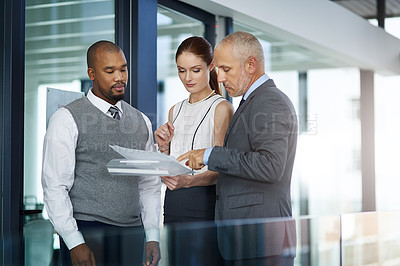 Buy stock photo Cropped shot of three businesspeople looking over paperwork in the office