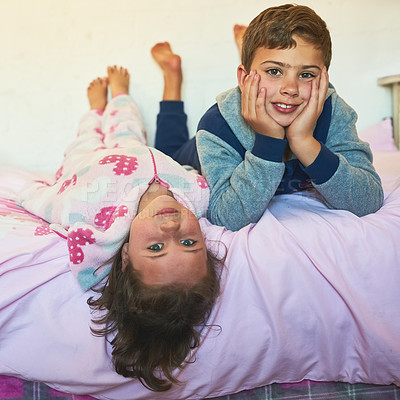 Buy stock photo Shot of two young siblings lying down together on a bed at home
